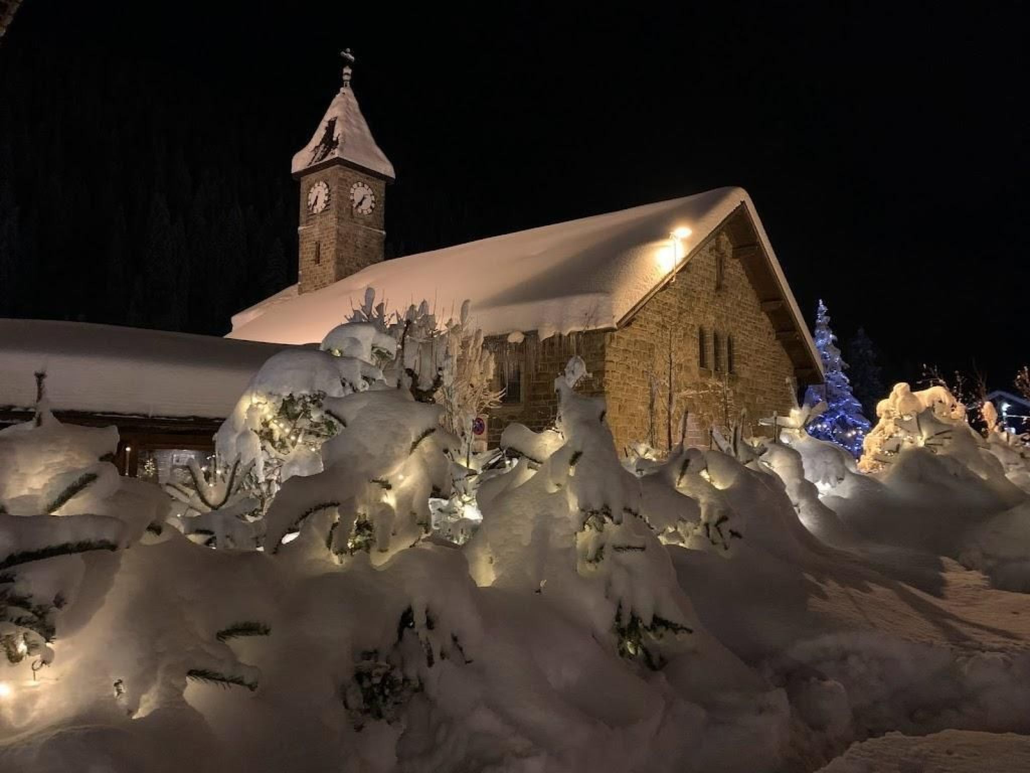A snow-covered building with a clock tower, surrounded by snow drifts and illuminated by artificial lights.