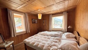 Una habitación de madera con una cama, dos ventanas, una silla y una lámpara.
