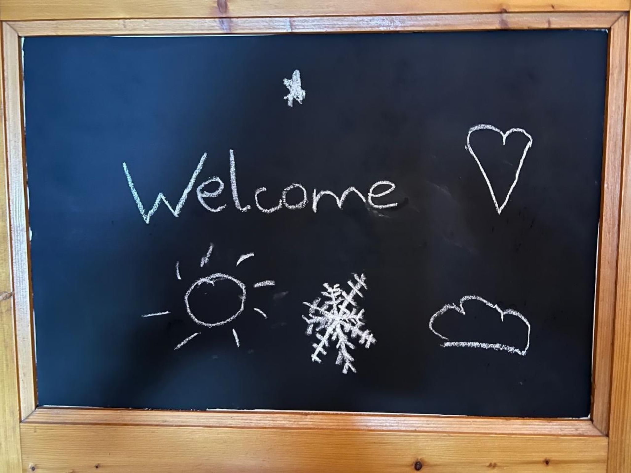 A blackboard with the word "Welcome" and a heart symbol, along with a sun, snowflake, and cloud drawing.