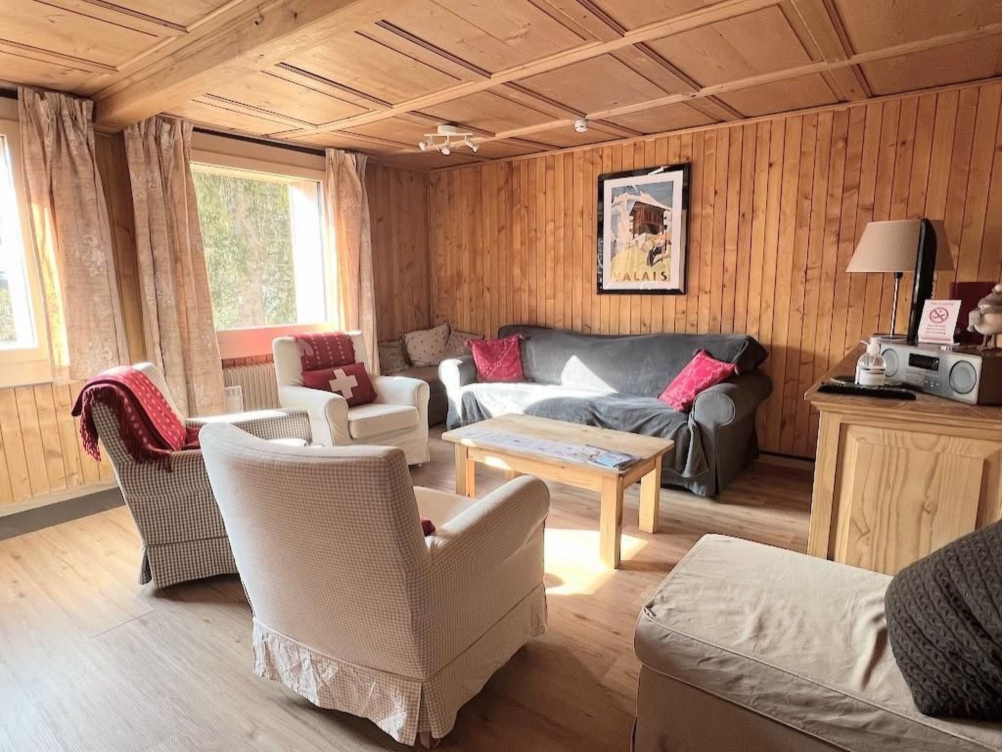 A cozy room with wooden walls, a sofa, a chair, a table, and a radio.