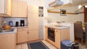 Une cuisine compacte dotée de meubles en bois, d’un four encastré, d’une machine à café et d’un coin repas avec une table et des chaises.