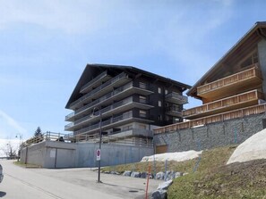 A multi-story building with balconies, a parking area, and a stone wall. - 3 Zi FeWo App 23. Le Miroi an Skipiste by Interhome (Les Crosets)