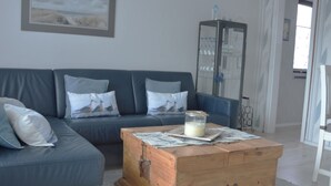 Uma sala de estar com um sofá azul, um baú de madeira e um quadro emoldurado na parede.