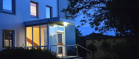 A modern building with a glass entrance, a staircase, and a tree in the background.