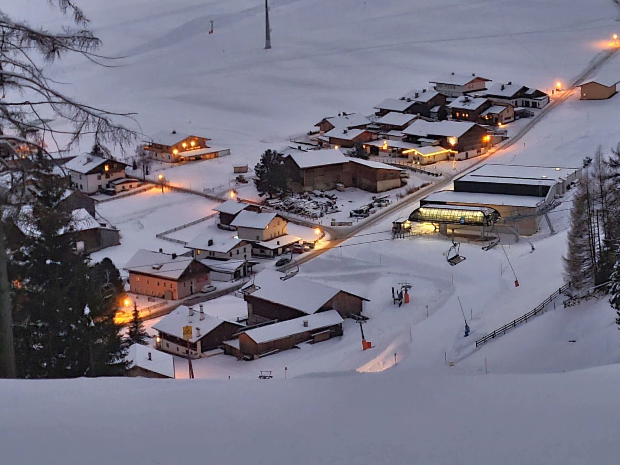 Ein schneebedecktes Dorf mit Häusern, einer Seilbahn und einer Straße.