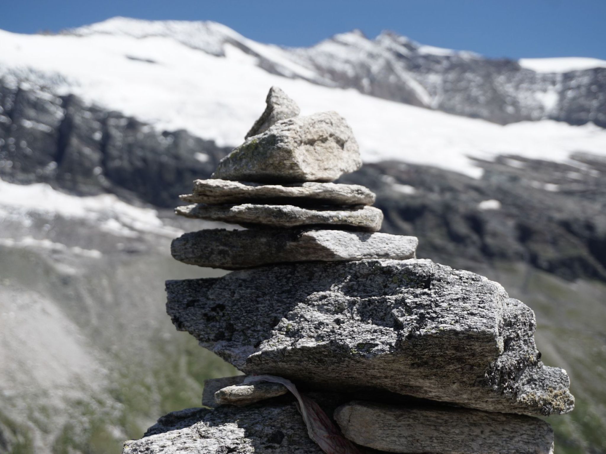 Una pila de rocas en una zona montañosa con picos nevados al fondo.