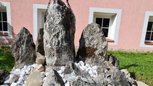 A cross on a rock with a solar panel, surrounded by stones and pink flowers, in front of a building with windows. - Osttirol by Interhome (Kals am Großglockner)