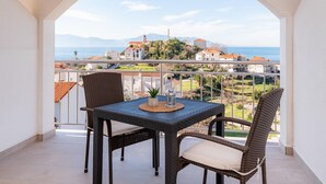 Un balcón con mesa y sillas, con vista a un pueblo costero y montañas a lo lejos.