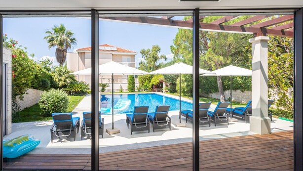 Ein moderner Poolbereich im Freien mit Liegestühlen und Sonnenschirmen, umgeben von Grünflächen und mit Blick auf ein Wohngebäude.