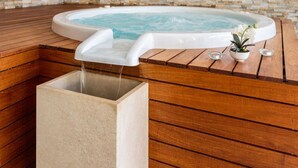 Ein moderner Wellnessbereich mit Whirlpool, Holzboden und Steinwand.