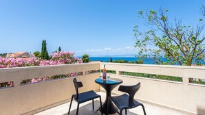 Ein Balkon mit zwei Korbstühlen und einem kleinen runden Tisch, mit Blick auf eine reizvolle Landschaft aus Meer und Bergen.