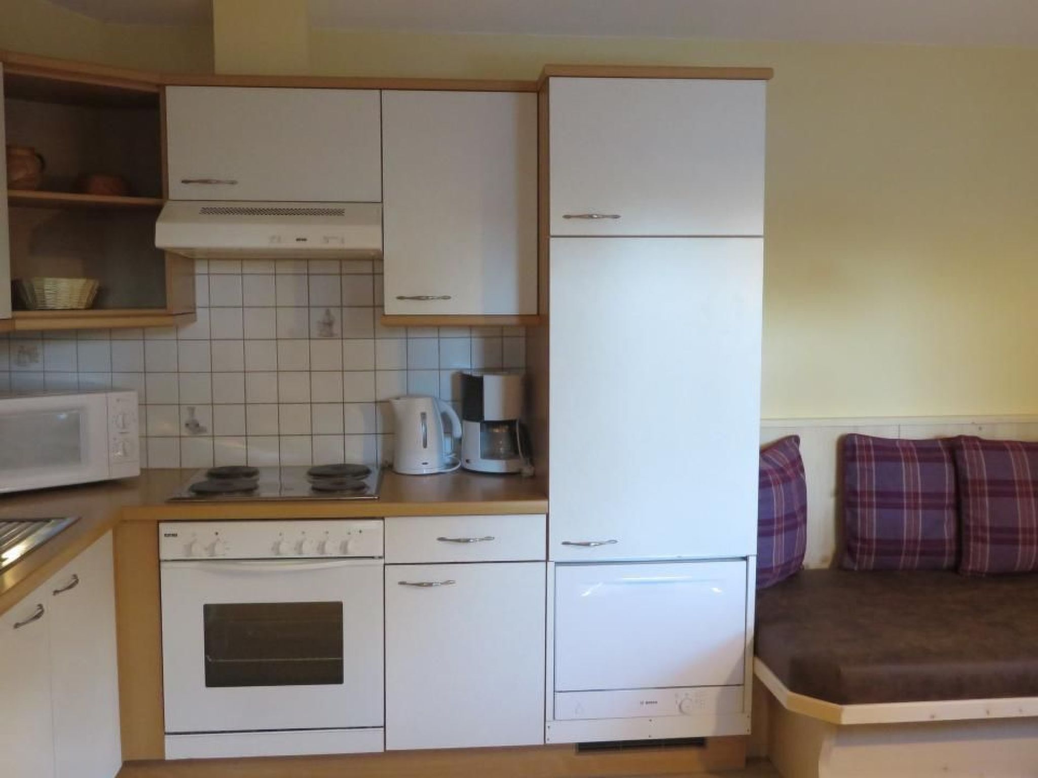 Een kleine keuken met witte apparaten, een magnetron, een koffiezetapparaat en een fornuis.