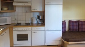 Eine kleine Küche mit weißen Geräten, einer Mikrowelle, einer Kaffeemaschine und einem Herd.