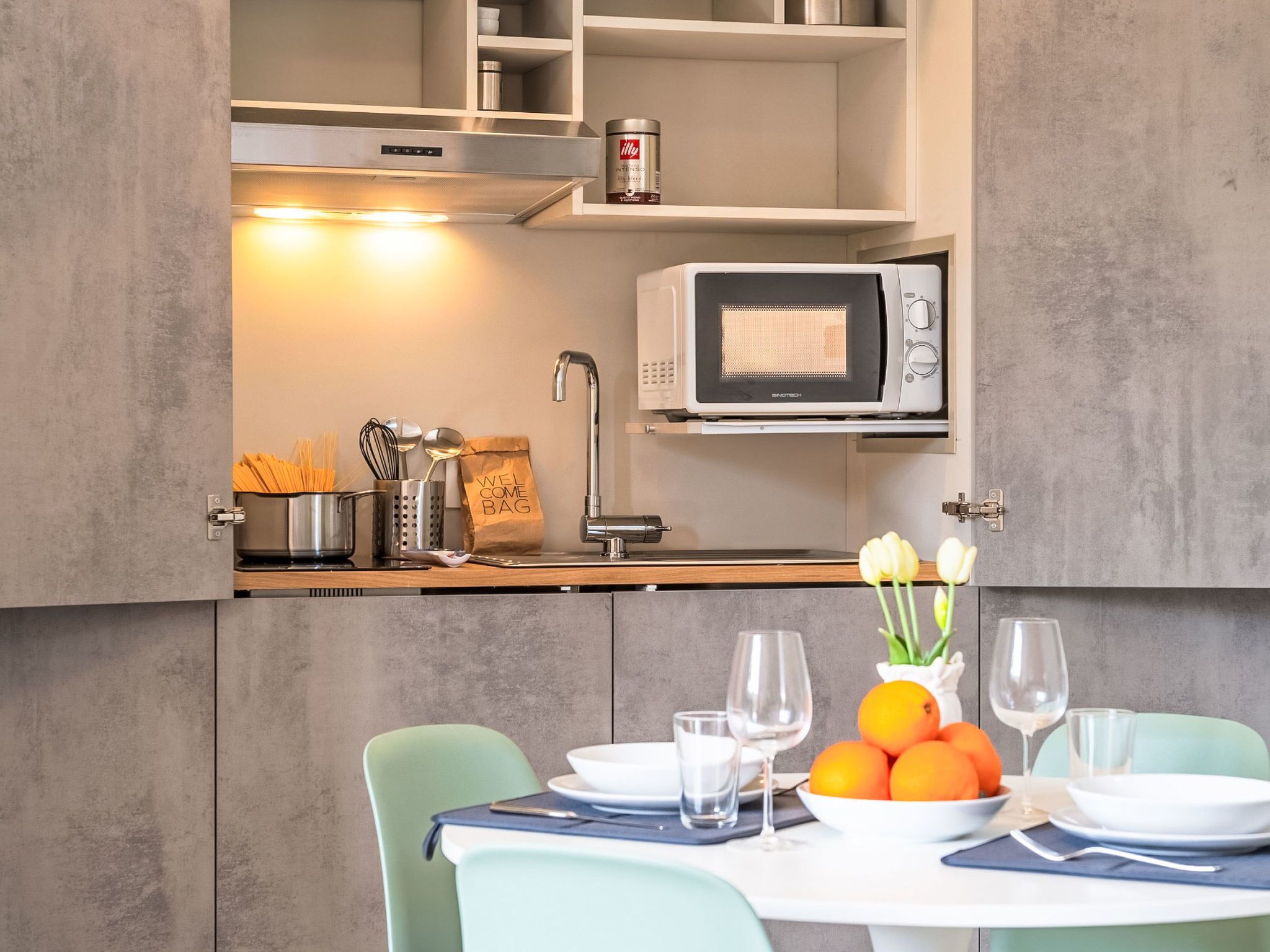 Una cucina moderna con microonde, utensili e una borsa di benvenuto sul bancone.