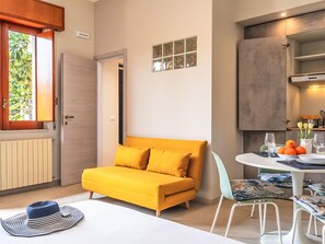 A compact room with a sofa, a dining table, and a window with a view of greenery. - Die Orange und der Goldfisch by Interhome (Calatabiano)