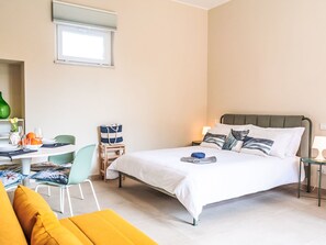 A hotel room with a bed, a desk with a chair, a small table with a lamp, and a window. - Die Orange und der Goldfisch by Interhome (Calatabiano)