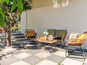 An outdoor patio with wicker furniture, a table with fruit and a vase, and a tree. - Die Orange und der Goldfisch by Interhome (Calatabiano)
