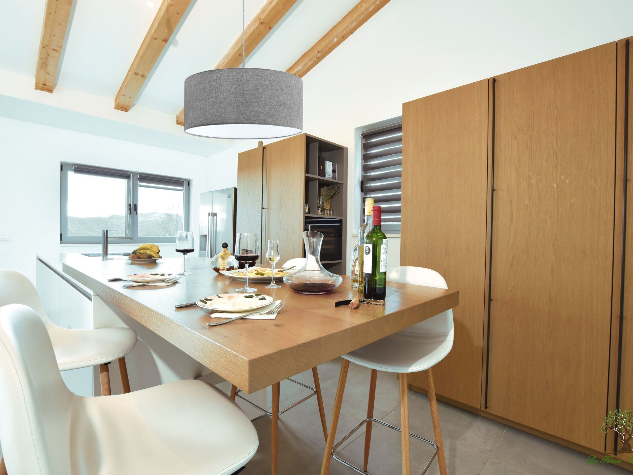 A modern kitchen with a wooden island, white chairs, and a hanging light fixture.