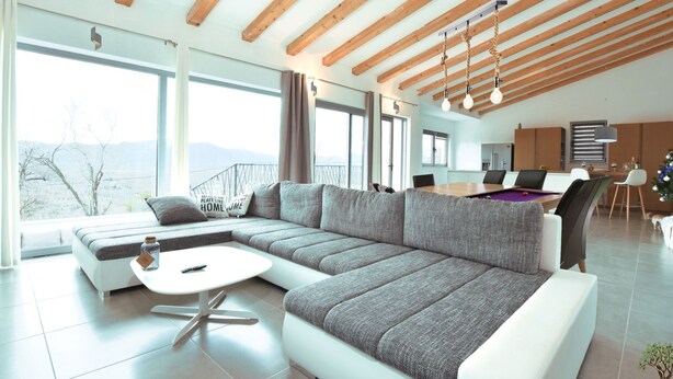 A modern living room with a large sectional sofa, a round coffee table, and a dining area with a wooden table and chairs. - La Finca OliveTree by Interhome (Katuni)