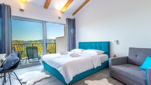 A modern bedroom with a large bed, a grey sofa, a desk, and a view of the mountains. - La Finca OliveTree by Interhome (Katuni)