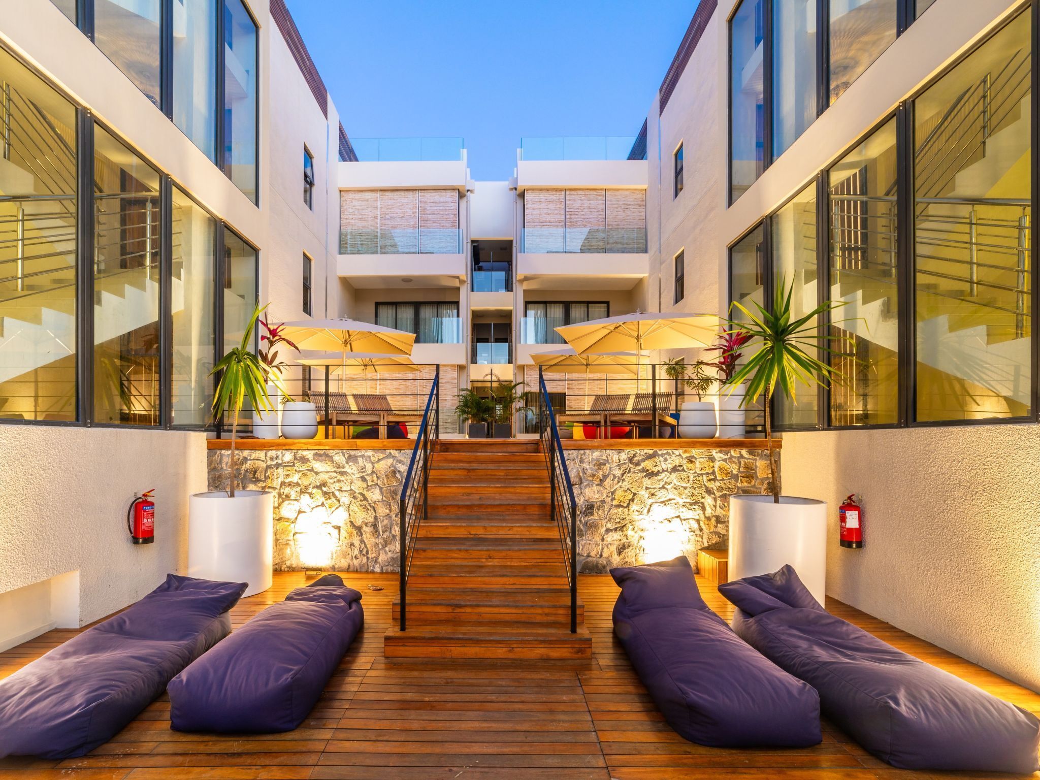 Un espacio lounge exterior moderno con suelo de madera, asientos y sombrillas.