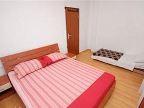 Ein kleines, ordentlich eingerichtetes Schlafzimmer mit einem Einzelbett, einem Holz-Kopfteil, einem kleinen Tisch und einer Tür.