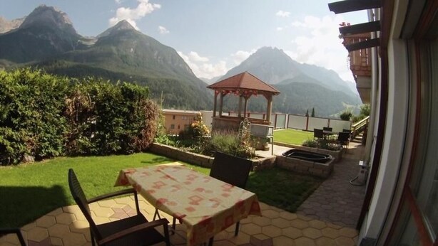 Eine Terrasse mit Tisch und Stühlen, ein Pavillon und Blick auf die Berge.