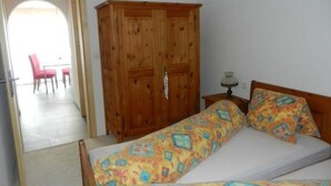 A bedroom with a wooden wardrobe, a bed with patterned bedding, and a small bedside table with a lamp. - Alvetern Marmotta by Interhome (Scuol)