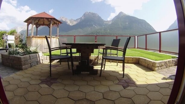 A patio with a hexagonal tiled floor, a wooden table with chairs, a wooden gazebo, and a view of mountains and a lake. - Alvetern Marmotta by Interhome (Scuol)