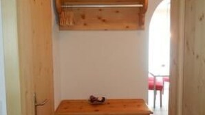 A wooden dresser with drawers and a shelf, a wooden door, and a window with a view of a red chair. - Alvetern Marmotta by Interhome (Scuol)