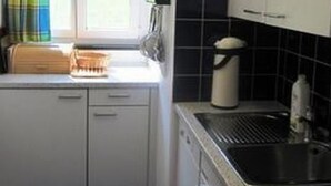 Cucina compatta con mobili bianchi, zoccolo a mosaico nero, finestra con tenda e lavello.