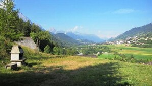 Paesaggio rurale con una costruzione in pietra, campi verdi e un villaggio in lontananza.