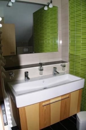A bathroom with a white sink, wooden cabinets, and a mirror with green-tiled backsplash.