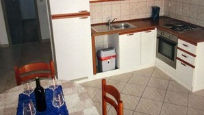 Et lille køkken med vask, komfur og skabe. Der er et spisebord med vinglas og en flaske vin.