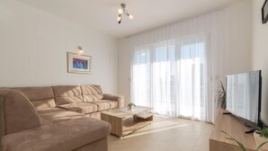 Een moderne woonkamer met een beige bank, een houten salontafel en een flatscreen televisie op een houten meubel.