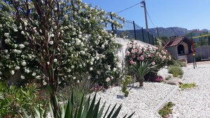 Een tuin met witte en roze bloemen, een rotstuin en een gebouw met een pannendak.