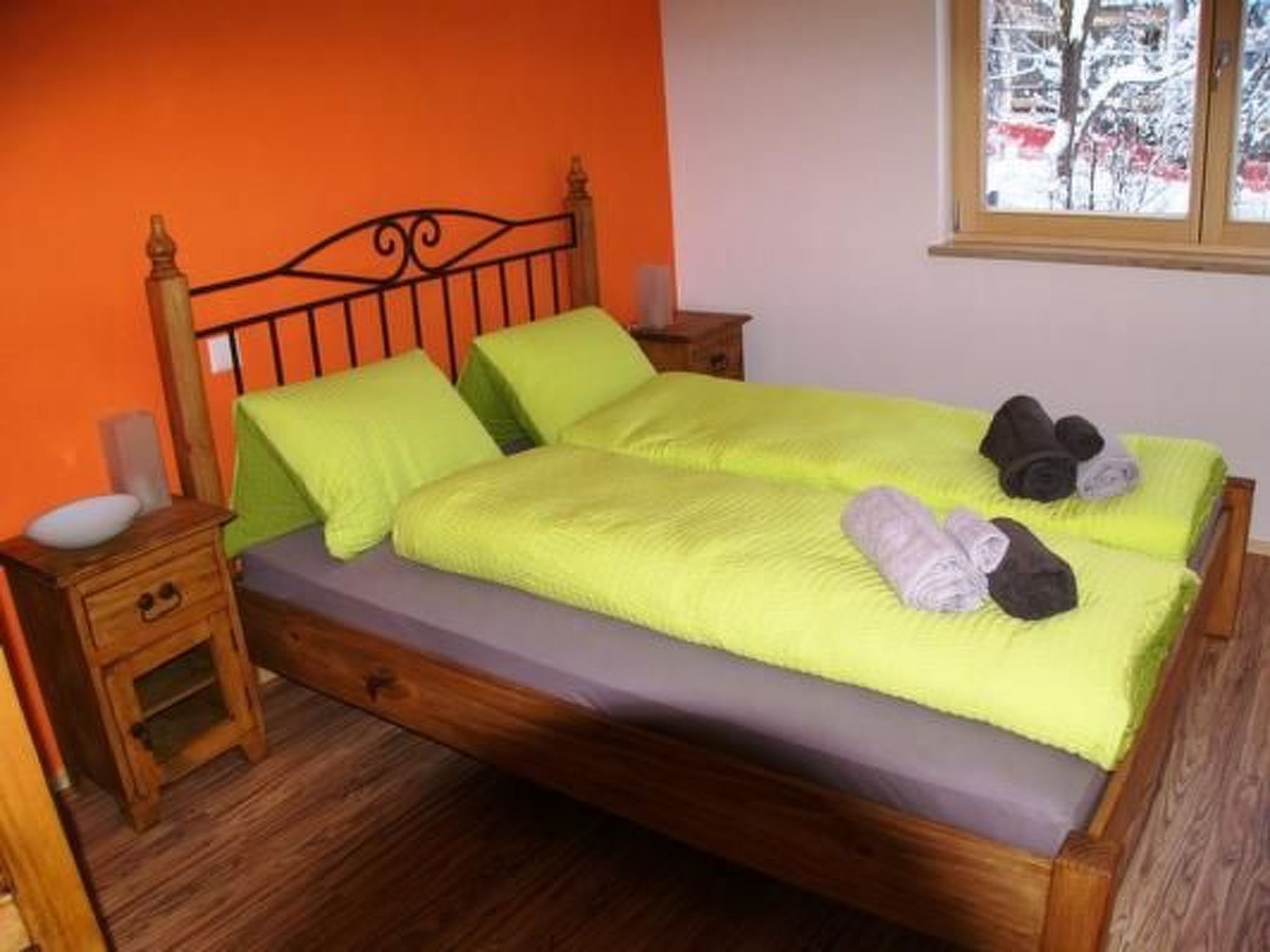 Un lit avec un cadre en bois, une couvre-lit verte et des oreillers. Il y a une table de chevet avec une lampe et un petit tiroir.
