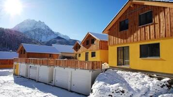 Une cabane en bois à la façade jaune, dotée d’une terrasse en bois et située dans un paysage montagneux.
