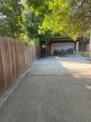 A covered patio area with a concrete floor, a wooden fence, and a garage in the background. - Cozy 1-bedroom studio in charming Los Angeles with AC (Los Angeles)