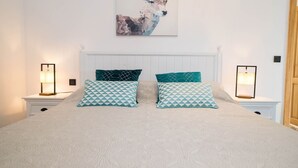 Un dormitorio con una cama blanca, dos almohadas iguales, cabecero y un cuadro abstracto colgado en la pared.