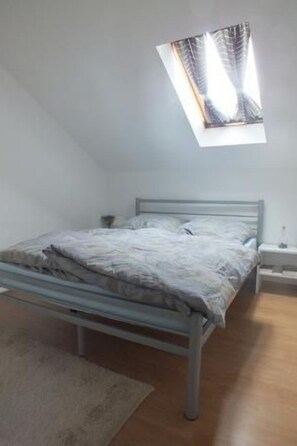 Een eenpersoonskamer met een schuine kap, dakraam, nachtkastje en bedtafel.