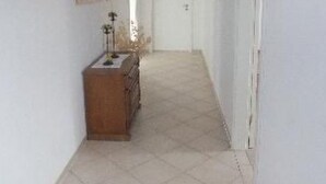 Ein schmaler Korridor mit Fliesenboden, einem Holzschrank und einer Tür am Ende.