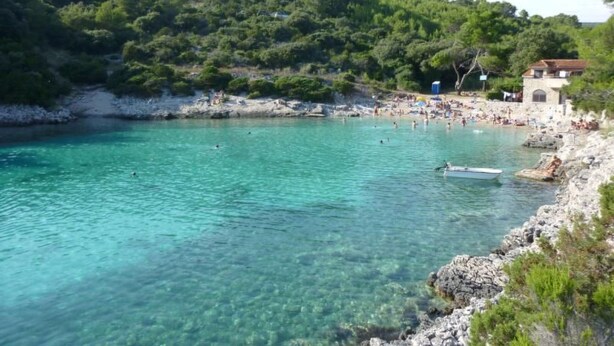 Eine Küstenlandschaft mit klarem türkisblauem Wasser, felsigen Ufern und einem kleinen Gebäude am rechten Rand.