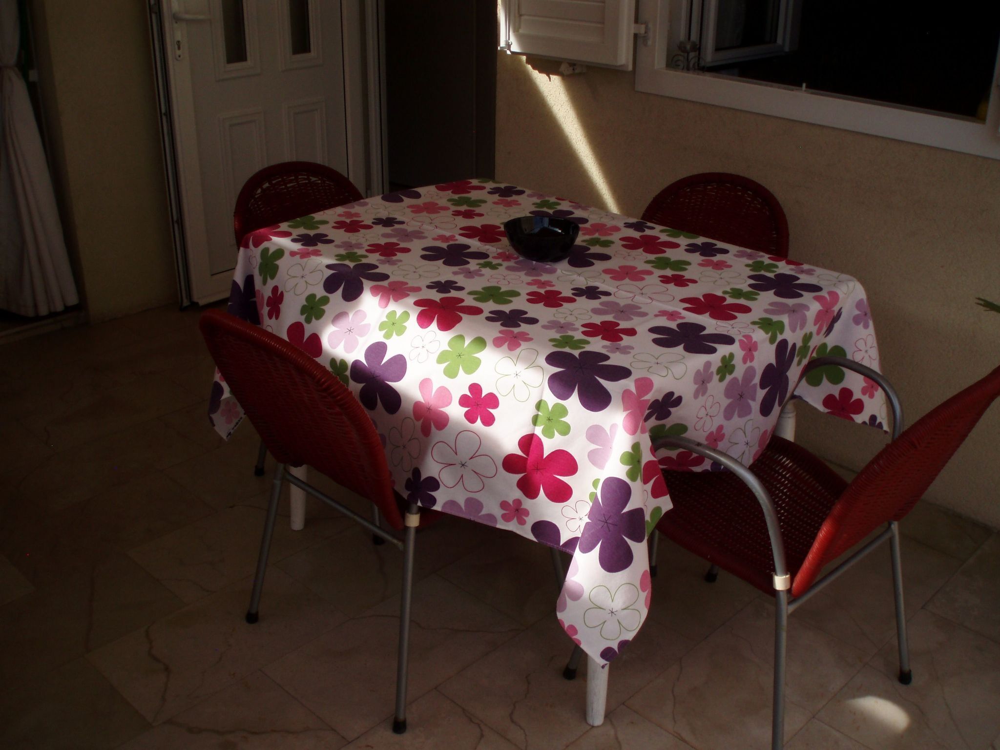 A dining table with a floral tablecloth, surrounded by four red chairs.