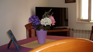 Uma mesa de jantar com um vaso roxo de flores, uma televisão e uma cadeira.