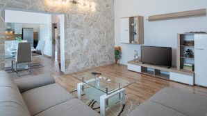 Ein modernes Wohnzimmer mit einer Wand aus Stein, einem Glastisch und einem Flachbildfernseher.