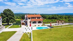 Ein zweistöckiges Haus mit Swimmingpool, umgeben von einer gepflegten Rasenfläche und Blick auf ferne Berge.