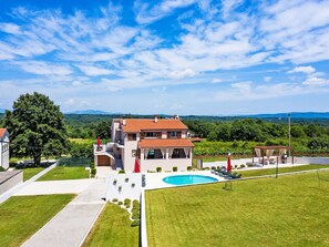 A two-story house with a swimming pool, surrounded by a well-maintained lawn and a view of distant mountains. - 3-Schlafzimmer-Wohnung mit Gemeinschaftspool by Interhome (Barban)