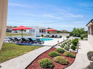 A swimming pool with lounge chairs and umbrellas, surrounded by a landscaped garden with various shrubs. - 3-Schlafzimmer-Wohnung mit Gemeinschaftspool by Interhome (Barban)