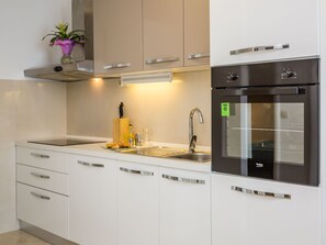 A modern kitchen with white cabinets, stainless steel appliances, a sink, and a small potted plant. - Große Wohnung in Omiš mit Möbliertem Balkon by Interhome (Omiš)